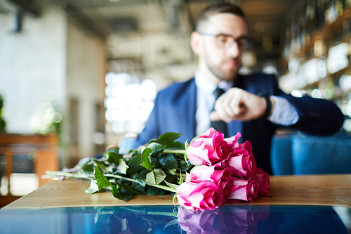 Bunch of pink roses on background of man waiting for his girlfriend by table