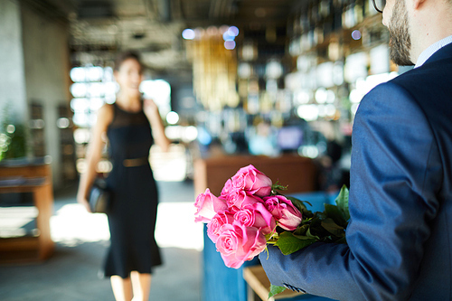 Fresh and romantic pink roses held by young man on background of moving woman in black dress