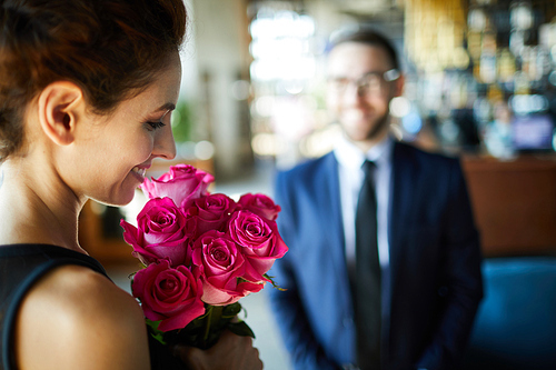Happy brunette woman looking at bunch of romantic pink roses from her boyfriend
