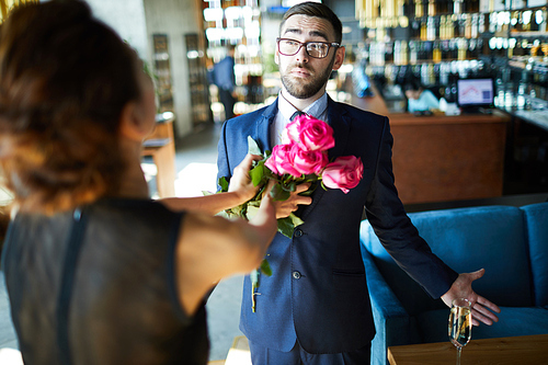 Confused or amazed elegant man looking at his girlfriend bumping bunch of pink roses to his chest
