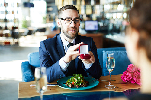 Young man in elegant suit offering girlfriend to be his wife during lunch in restaurant