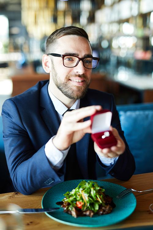 Happy young man showing engagement ring to his girlfriend by lunch in restaurant