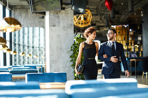 Amorous couple in elegant formalwear moving inside modern restaurant and talking