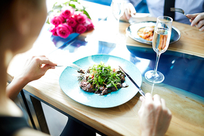 Young woman having meat salad with vegs while sitting by served table during romantic date with her boyfriend