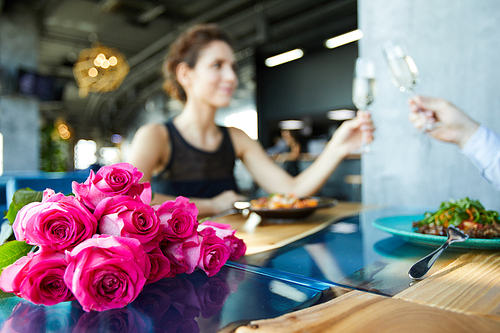 Fresh pink roses on table on background of amorous couple toasting for love with champagne