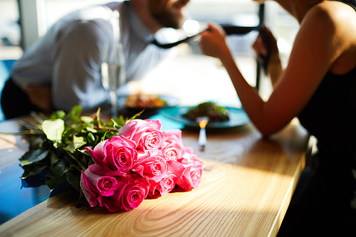 Fresh romantic roses on table on background of amorous man and woman flirting