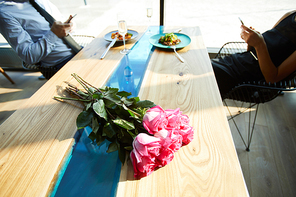 Fresh pink roses on table with served food and couple addicted to gadgets on background