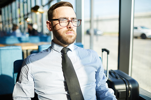 Bearded man in formalwear and eyeglasses sitting in restaurant by window on sunny day