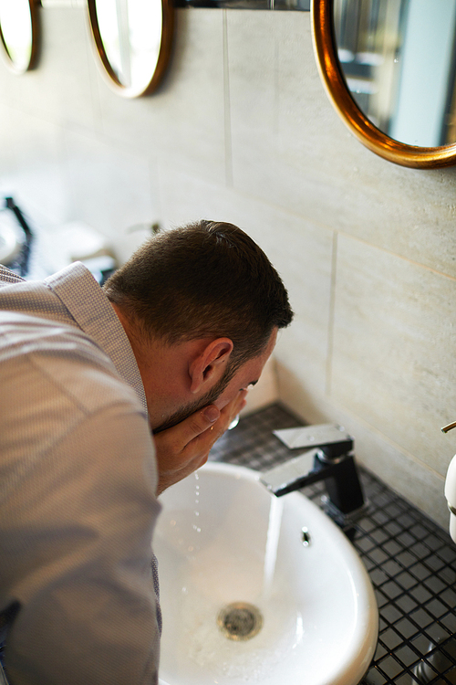 Tired or sleepy businessman refreshing with cool water over sink in bathroom of airport