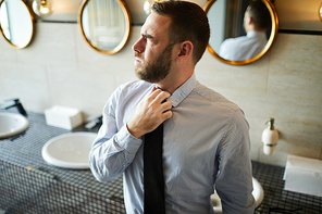 Businessman loosing his tie while visiting lavatory in airport before flight