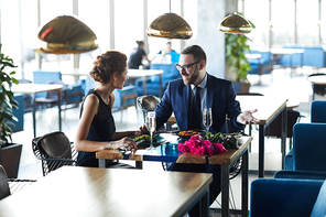 Happy man in suit talking to his girlfriend by romantic lunch in modern restaurant