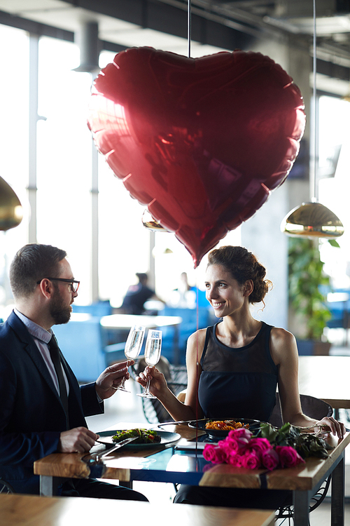 Happy amorous couple clinking by flutes of champagne while enjoying romantic date in restaurant