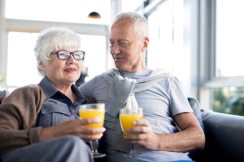 Portrait of modern senior couple embracing and holding glasses with fresh orange juice while enjoying breakfast in cafe at Sea resort