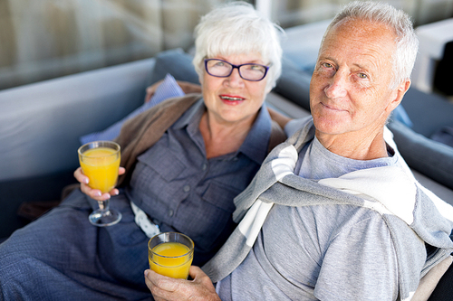 High angle portrait of modern senior couple embracing and holding glasses with fresh orange juice while enjoying breakfast in cafe at Sea resort
