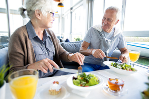 Portrait of modern senior couple enjoying lunch and conversation on vacation in resort cafe