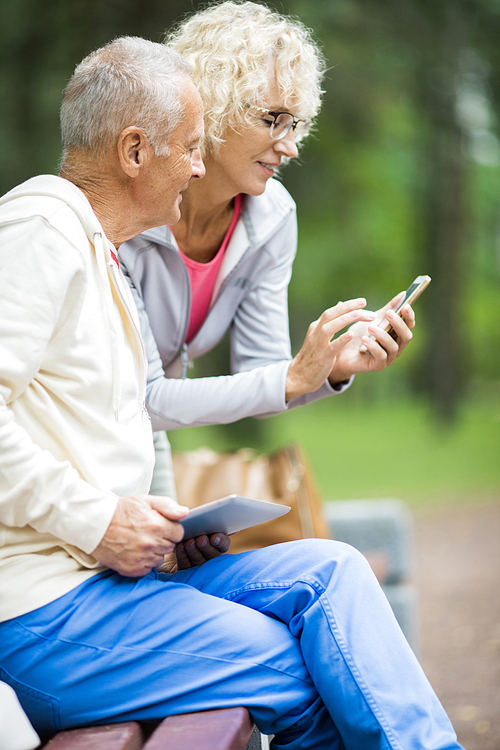 Modern seniors with mobile gadgets looking through online pics or videos in park