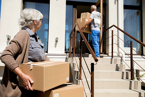 Portrait of modern senior couple unloading cardboard boxes while moving to new house, copy space