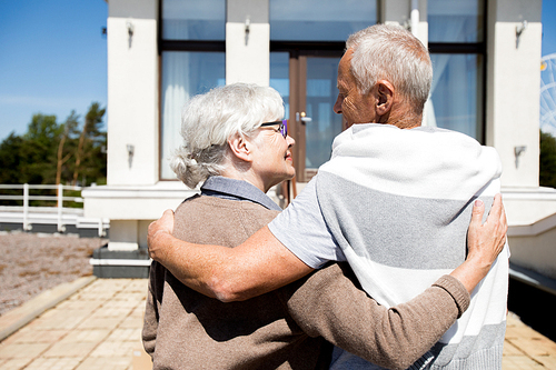 Back view portrait of modern senior couple embracing outdoors in sunlight smiling happily