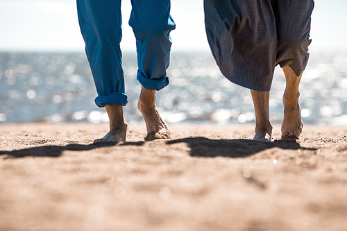 Bare foot of senior couple taking walk on sandy beach on sunny day