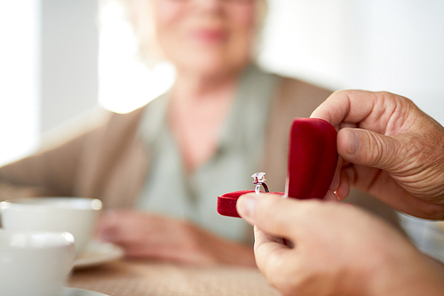 Senior man holding red velvet box with engagement ring while making surprise for mature woman