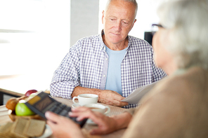 Mature man with papers and his wife with calculator counting their expenses