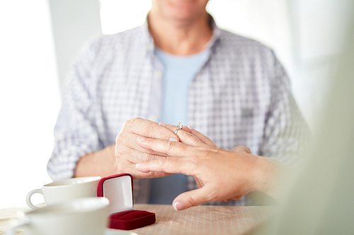 Mature husband putting diamond ring on his spouse finger during celebration of anniversary