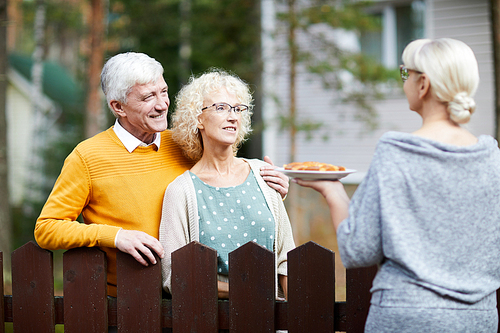 Mature woman giving her new neighbours homemade fresh apple pie on plate over fence