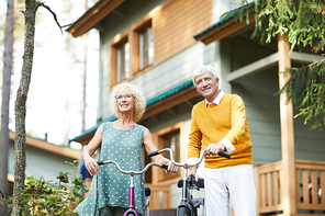 Mature casualw couple with bicycles going for chill in the forest on background of their country house