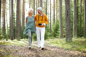 Happy mature man and woman in casualwear walking down forest pathway and enjoying summer day