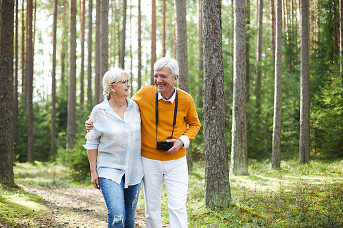 Laughing senior couple taking walk in the forest on summer day, talking and enjoying their chill