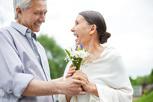 Surprised senior woman taking bunch of beautiful flowers from her husband hands