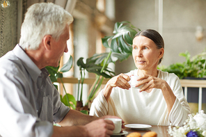 Two senior adults with cups of tea having talk while relaxing in cafe after walk