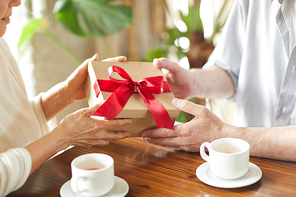 Senior man holding packed carton box with red bow on top and giving it to his wife for birthday or other occasion