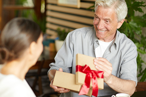 Happy senior man opening giftbox with present from his wife and looking at her