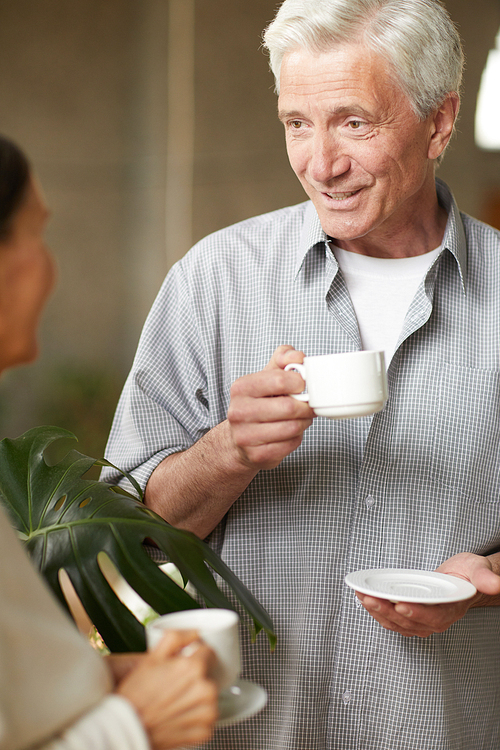 Senior man with cup of tea or coffee talking to his wife at coffee-break in cafe