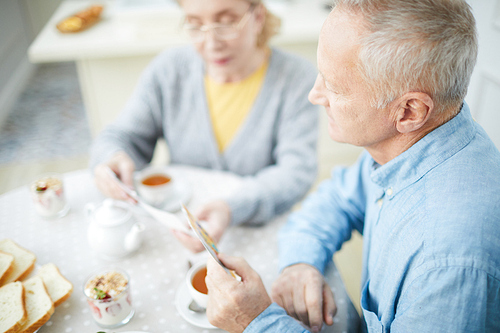 Senior man with frey hair and his wife looking through pictures by breakfast