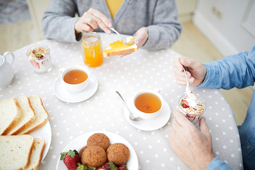 Tea-time idyl of senior couple with cups of herbal tea, cream dessert, cookies and toasts with jam