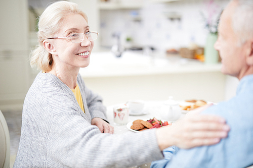 Smiling pretty senior wife somforting her husband by served table during breakfast