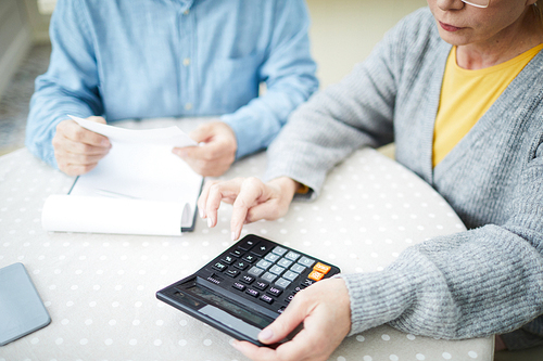 Senior wife with calculator counting all expenses of the last month with her husband near by