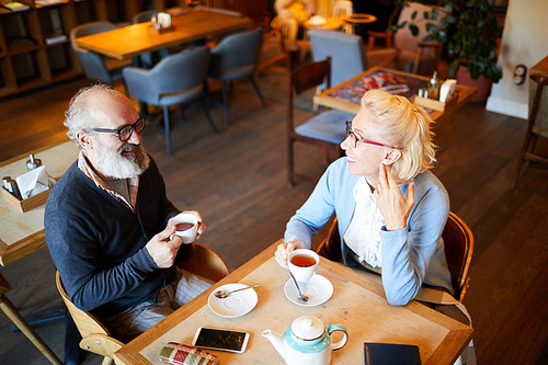 Happy mature couple in casualwear sitting by table in cafe, having tea and chatting