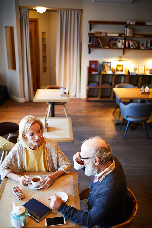 Senior man drinking tea while sitting by table in front of his colleague during work planning