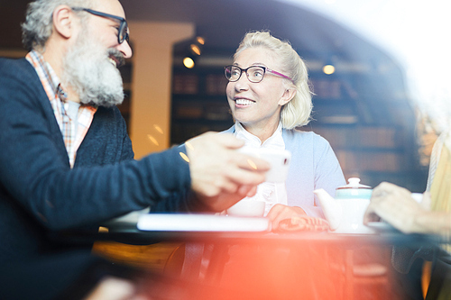 Happy blonde mature woman and her friend discussing their idea by cup of tea