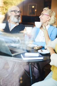 Group of cheerful seniors having tea and discussing curious news at meeting in cafe