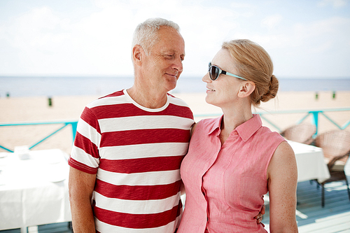 Happy senior spouses looking at each other at summer resort while spending day close to beach