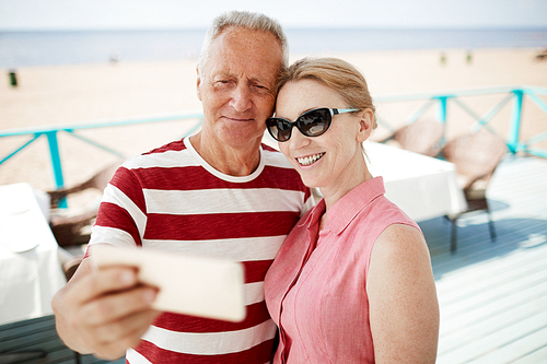 Cheerful amorous mature man and woman making selfie with smartphone camera while enjoying summer vacation