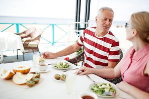 Aged couple sitting by served table, having breakfast and talking at summer resort outdoor cafe