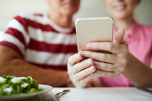 Smartphone held by mature female over served table during communication in video-chat