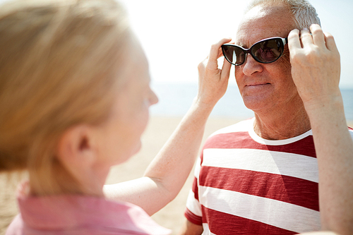 Aged woman trying her sunglasses on husband during their rest on summer vacation