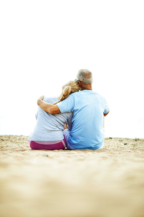 Back view of affectionate senior couple sitting on sand in embrace and relaxing after workout
