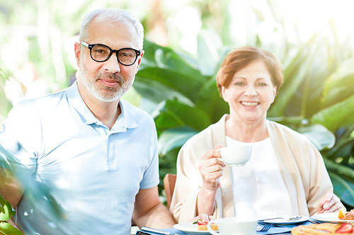 Aged couple  while sitting by served table and having breakfast in their home garden